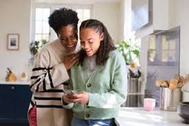 Black mother and teenage daughter smiling while looking at a smartphone together, building trust